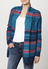 Modrý pletený cardigan s geometrickými vzory v tmavě modré a růžové barvě, otevřený přední design a žebrované manžety a lem. Měkká textura.