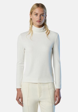 Maglione bianco a collo alto con costine e maniche lunghe, texture uniforme e accento di logo discreto sul lato, abbinato a pantaloni color crema.