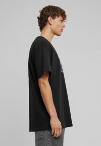 Sort bomulds T-shirt med afslappet pasform, rund halsudskæring, korte ærmer og grafisk detalje foran. Glat tekstur og enkelt snit.