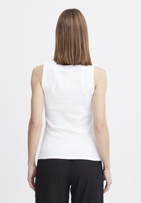 Weißes geripptes Tanktop mit rundem Ausschnitt und breiten Schulterträgern, kombiniert mit lockeren schwarzen Hosen. Glatte Textur und figurschmeichelnde Passform.