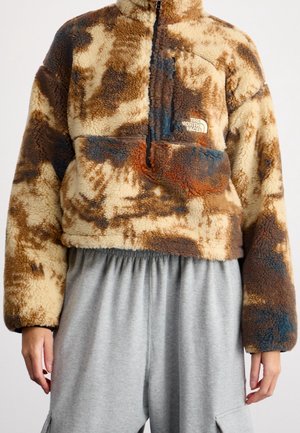 Hnědo-béžová fleecová bunda s batikováním, s kapsou na zip na hrudi, ve spojení s volnými šedými kalhotami s elastickým pasem.