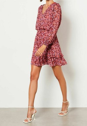 Jurk met bloemenprint, v-hals, lange mouwen en een gelaagde rucheszoom. Roze, paars en groene tinten. Gecombineerd met witte sandalen met bandjes.