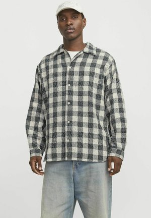 Black and white checkered button-up shirt with a collar, long sleeves, and textured fabric, paired with light denim jeans.