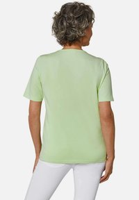 T-shirt verde chiaro con maniche corte, scollatura rotonda e una texture liscia. La vista dal retro mostra un design aderente.