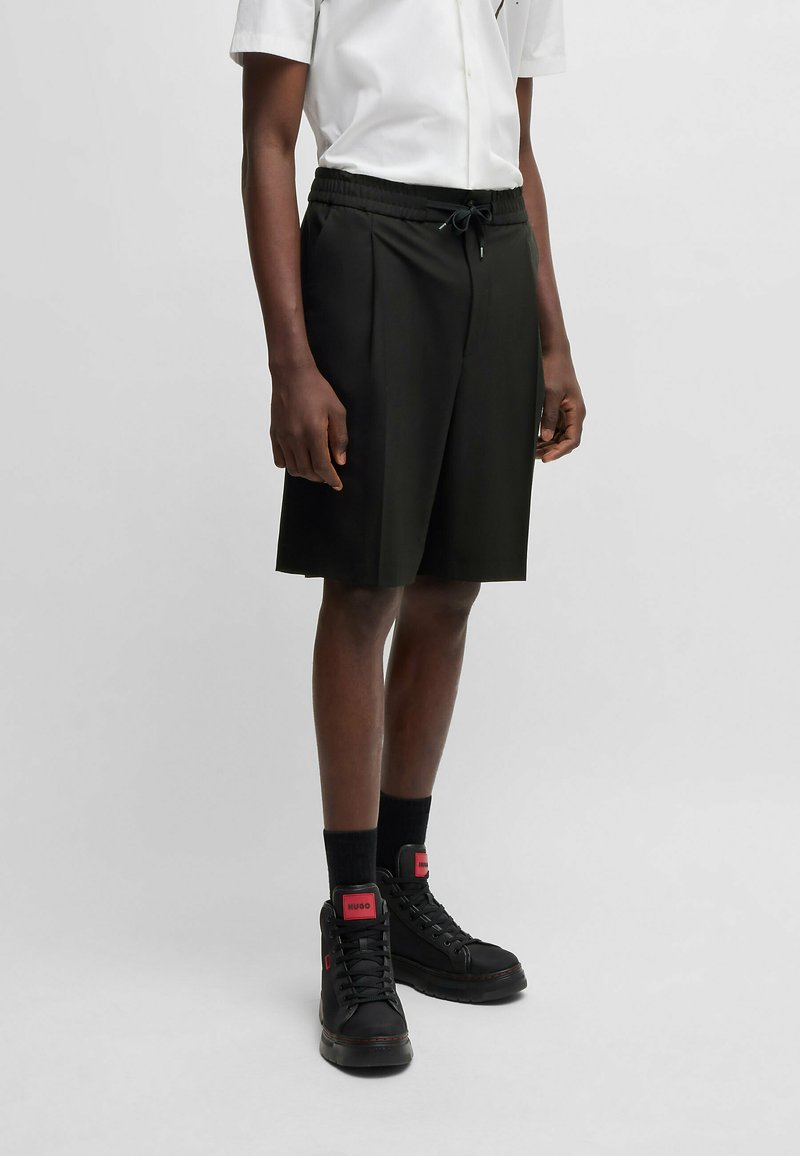 Black knee-length shorts with an elastic waistband and drawstring. Paired with black high-top sneakers featuring red accents.