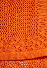 Oranžová textilie s otevřeným pletením, která má na spodním okraji diamantový vzor a na lemu hladký ribbed povrch, zdůrazňující svou živou barvu.