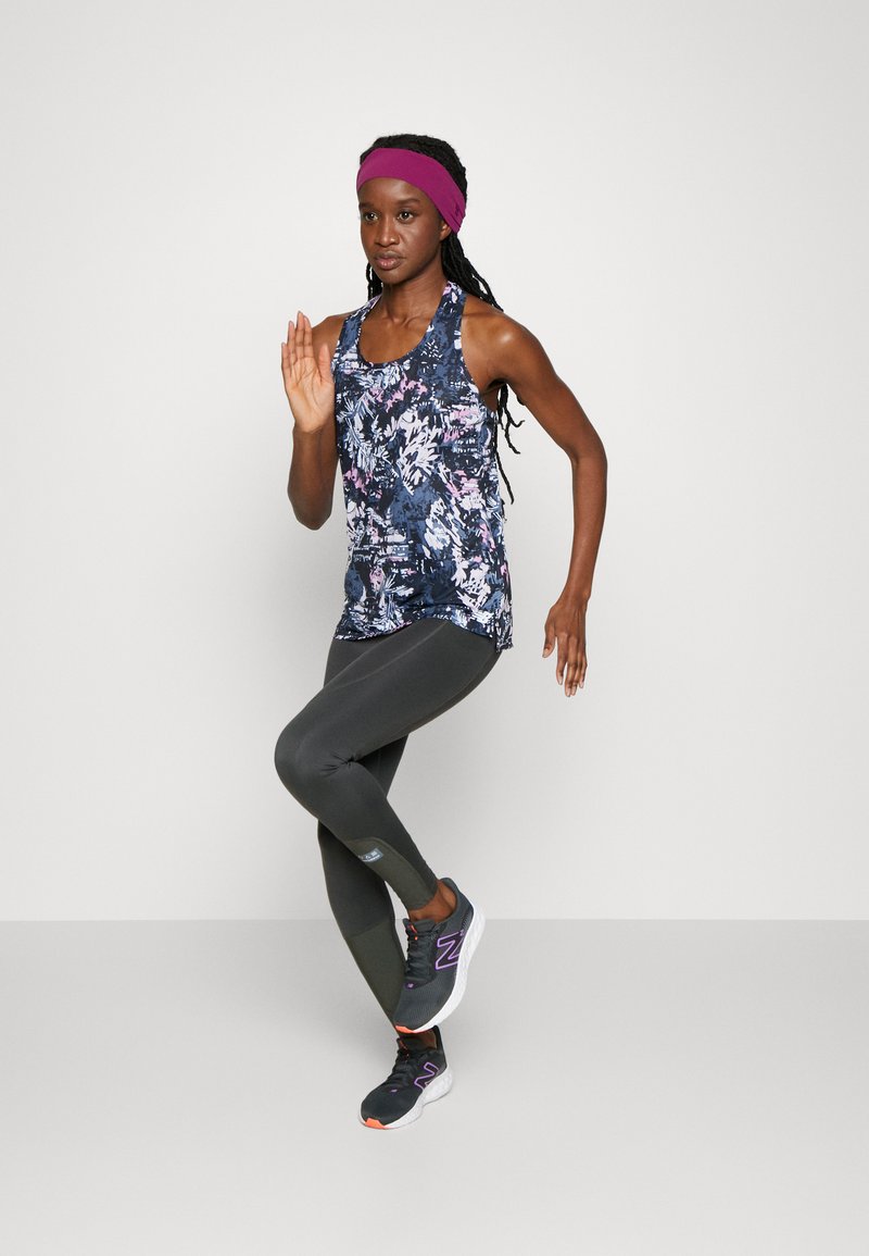 Tenue de sport composée d'un haut à motif floral sombre, de leggings vert olive et de chaussures de sport noires avec des accents violets. Bandeau bordeaux.