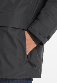 Black waterproof jacket featuring a zippered side pocket and adjustable cuffs; smooth texture and modern design.