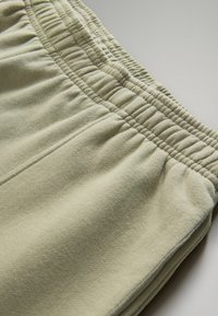 Pantaloni della tuta verde chiaro con elastico in vita arricciato, tessuto morbido e una sottile cucitura lungo le cuciture.