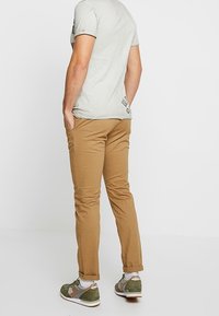 Camiseta de manga corta gris claro, pantalones slim-fit beige y zapatillas verdes con suela blanca, visto desde atrás. Sin patrones o acentos notables.