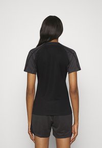 Top deportivo negro de manga corta con hombros y espalda texturizados y con patrón, combinado con pantalones cortos negros que presentan un sutil diseño geométrico.