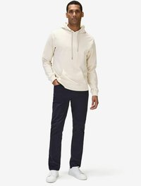 Krämm hoodie med dragsnören, kenguruficka, i kombination med marinblå byxor och vita sneakers. Slät material, avslappnad passform, minimalistisk design.