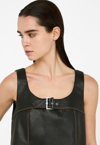 Top in pelle nera con scollatura quadrata, caratterizzato da un prominente dettaglio in fibbia argentata e da una cucitura in tinta marrone a contrasto lungo le cuciture.