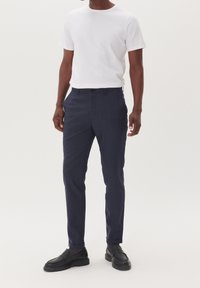 Marinblå slim-fit byxor med ett subtilt rutmönster, tillsammans med en enkel vit t-shirt med rund halsringning och svarta slip-on skor.