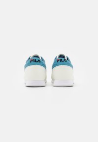Blå och vita sneakers med ovandel i slät läder, vadderad krage, vit sula och röd logodetalj på hälen. Enkelt, atletiskt design.