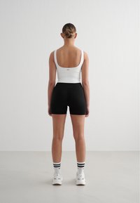Hvit ribbet tanktop med firkantet rygg, kombinert med svarte ribbet shorts. Modellen har på seg hvite joggesko med svarte stripete sokker.