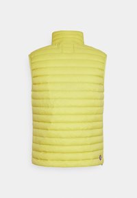 Ljust gul vadderad ärmlös väst med hög krage, horisontell sömnad och liten rund logotyp nära nederkanten mot en enkel bakgrund.