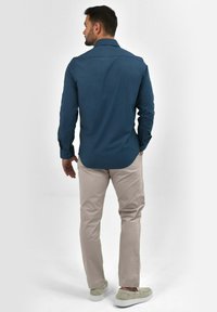 Blauwe overhemden met lange mouwen en een knoopsluiting kraag, gecombineerd met lichtbeige broeken en grijze instapschoenen. Gladde stof, casual pasvorm.