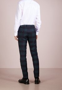 Pantalones a cuadros con un patrón de cuadros en verde oscuro y azul marino, diseño ajustado y dos bolsillos traseros. Combinados con una camisa blanca.
