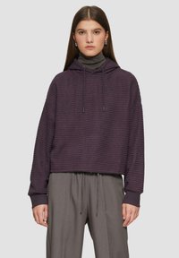 Paarse hoodie met verticale geribbelde textuur, cropped ontwerp en capuchon met koord. Gecombineerd met grijze high-waisted broek.