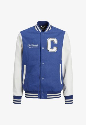 Veste de varsity bleue avec des manches crème, lettres "C" brodées, poignets rayés ; associée à un pantalon noir et des baskets bleu et blanc.