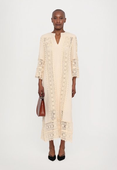 Beige midi dress with lace detailing, V-neckline, and three-quarter sleeves. Paired with a brown handbag and black pointed-toe shoes.