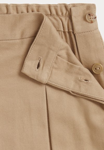 Beige bukser med teksturert stoff, elastisk midjebånd og knappelukking med subtile folder og dobbeltsøm detaljer.