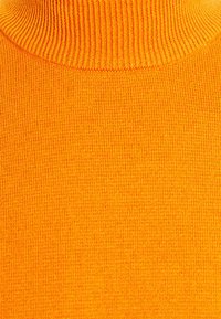 Oranger Rollkragenpullover mit einem Rippdesign. Die Stricktextur ist glatt, mit engen Stichen, die ein gemütliches Aussehen erzeugen.