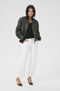 Nő zsebébe tett kézzel, sötétszürke bomberdzsekit, fekete felsőt, fehér bő szárú nadrágot és fekete hegyes orrú magassarkút viselve.