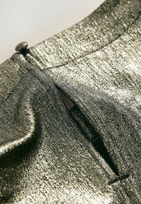 Glanzende metallic stof met een gestructureerde afwerking, met een knoopdetail en een kleine opening. De kleur is een mix van zilver en donkergrijs.
