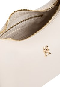 Τσάντα χειρός από κρεμ δέρμα με χρυστό φερμουάρ και εσωτερική τσέπη με φερμουάρ, με μικρό χρυσό λογότυπο Tommy Hilfiger στο μπροστινό μέρος.