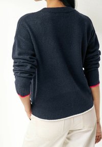 Pull tricoté bleu marine avec ourlet et poignets côtelés ; présente des accents roses sur les manches, une coupe décontractée et un tissu texturé.