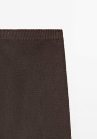 Tissu tricoté côtelé marron foncé avec une ceinture élastique, probablement une partie d'une jupe ou d'un pantalon, sur un fond blanc uni.