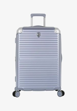 Valise rigide argentée avec des rainures horizontales, quatre roues pivotantes et une poignée télescopique étendue.
