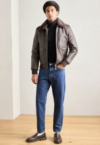 Brown leather bomber jacket with a fur collar, paired with blue denim jeans and dark brown shoes. Simple design, fitted silhouette.
