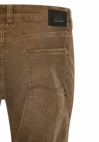 Bruine corduroy broek heeft een achterzak met een gebogen naad en een zwart merkelabel op de tailleband. De textuur is ribbelig en duurzaam.