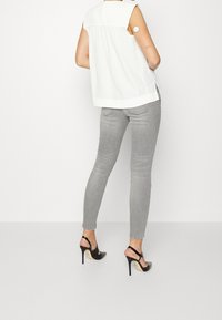 Top blanco sin mangas con la parte de atrás fruncida, combinado con jeans ajustados grises y zapatos de tacón negro con una correa en el tobillo.