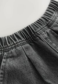 Grauer Denim-Stoff verfügt über einen elastischen Bund mit gerafften Nähten. Die Textur ist glatt mit sichtbarem Webmuster und leichtem Glanz.