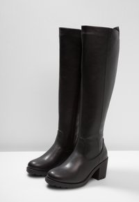 Para wysokich, czarnych skórzanych botków na słupku, z zaokrąglonymi noskami i bocznymi zamkami, umieszczonych na białej powierzchni na szarym tle.