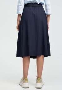 Marinblå midijupe med en samlad midja och subtil textur, i kombination med ljusa sneakers med neondetaljer.