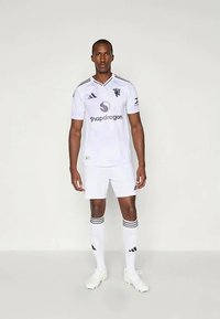 Άσπρη ποδοσφαιρική στολή με μαύρες λεπτομέρειες, που διαθέτει V-λαιμό, λογότυπο στο στήθος και κάλτσες με μαύρες ρίγες. Φοριέται με άσπρα παπούτσια ποδοσφαίρου.