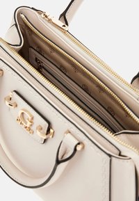 Borsa a tracolla in pelle beige con dettagli in oro, chiusura con zip superiore e tasche interne. Presenta un dettaglio con logo e rifiniture in nero a contrasto.