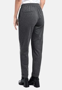 Graue schmal zulaufende Hosen aus strukturiertem Stoff mit elastischem Bund, ausgestattet mit einer Gesäßtasche, getragen mit schwarzen Absatzstiefeletten.