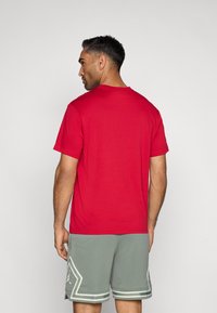 Κόκκινη βαμβακερή μπλούζα με κοντά μανίκια, συνδυασμένη με γκρι αθλητικές βερμούδες από πλέγμα με λευκές λεπτομέρειες και σπορ σχέδιο.