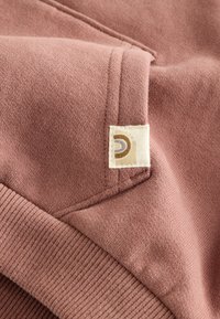 Felpa rosa polveroso con polsini e orlo a coste, con una piccola etichetta color crema con un logo circolare in marrone e beige.