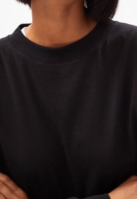 Schwarzes Sweatshirt aus weichem Baumwollmaterial, mit Rundhalsausschnitt, langen Ärmeln und einem kleinen Logoakzent auf der Brust. Weiche Textur.