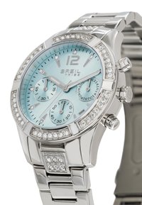 Montre ton argent avec un cadran bleu clair, des accents en cristal, des sous-cadrans chronographes et un bracelet en métal poli.