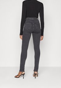 Höga svarta denimjeans med smal passform, med bakfickor och sprund vid anklarna. Bärs med svarta strappy klackar.