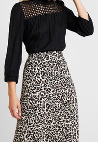 Schwarze Bluse mit langen Ärmeln, einer strukturierten Spitzenblende und Falten.Detail, kombiniert mit einem Maxirock im Beige- und Schwarz-Leopardenmuster.