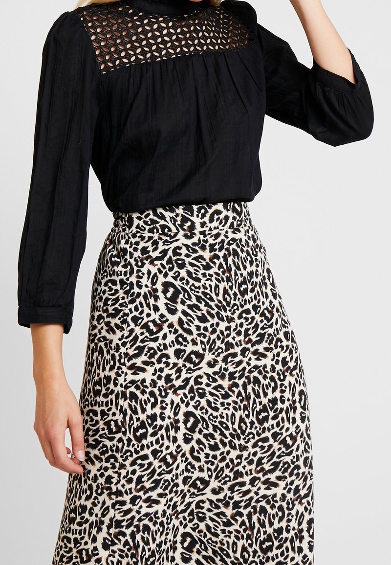 Schwarze Bluse mit langen Ärmeln, einer strukturierten Spitzenblende und Falten.Detail, kombiniert mit einem Maxirock im Beige- und Schwarz-Leopardenmuster.